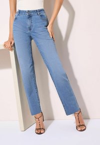 Heleda sinine kõrge vöökoha ja sirge sääre disainiga teksad, millel on ees taskud ja õrn fading, kombineeritud mustade rihmadega kontsakingadega.