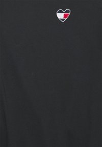Czarna bawełniana koszulka z małym haftowanym logo serca w czerwono-biało-niebieskich detalach, umieszczona po lewej stronie klatki piersiowej.