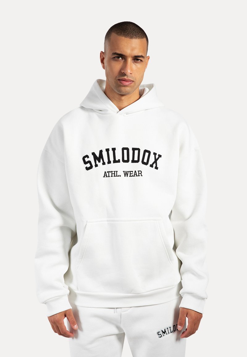 Sweat à capuche blanc avec une poche avant et des poignets côtelés, arborant "SMILODOX ATHL. WEAR" en lettres noires sur la poitrine.