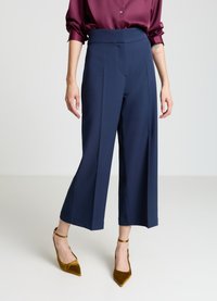 Pantalon large marine à taille haute, texture lisse et plis centraux, associé à des talons pointus en velours et un chemisier bordeaux.