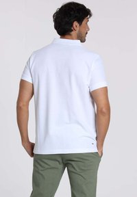 Polo shirt blanc à manches courtes, en coton, col classique, vue de dos, associé à un pantalon vert clair, design minimal sans motifs.