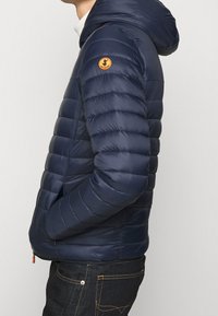 Marineblauwe donsjack met capuchon, met horizontale stiksels, een zijrits en een klein logopatch op de bovenarm.