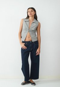 Bezramionowa, w paski bluzka z węzłem na środku; zestawiona z luźnymi, ciemnoniebieskimi spodniami dżinsowymi i błyszczącymi srebrnymi balerinkami.