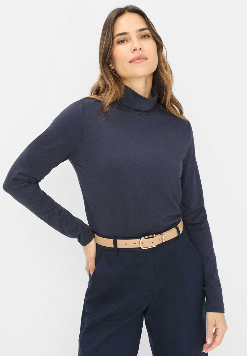 Navy langærmet turtleneck skjorte lavet af blødt stof, med et tætsiddende design, kombineret med højderetstående mørke bukser og et beige bælte.