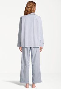 Sininen ja valkoinen raidallinen pyjama, jossa on pitkähihaisella napitettavalla paidalla ja leveälahkeisilla housuilla, jotka ovat sileätekstuurisia ja joissa on kontrastoivat hihansuut.