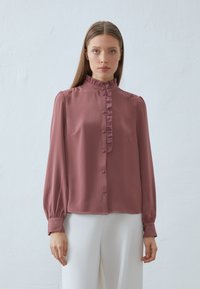 Blusa rosa realizzata in tessuto liscio, con placca volante, maniche lunghe con polsini a bottone e vestibilità comoda.