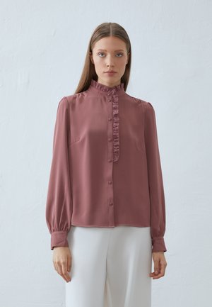 Rosa bluse laget av glatt stoff, med volangdetaljer, lange ermer med knappemansjetter og en avslappet passform.