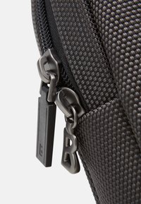 Schwarzer, strukturiertes Stoff-Rucksack mit einem Reißverschlussdetail. Ausgestattet mit Metall-Reißverschluss-Ziehgriffen und einem sichtbaren Stichmuster entlang der Kante.