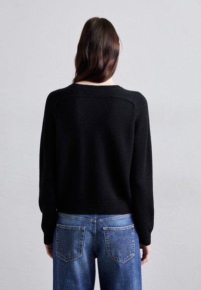 Pulover negru tricotat cu guler rotund, manșete ajustate și un design scurt, asortat cu blugi albaștri cu buzunare din spate distinctive.