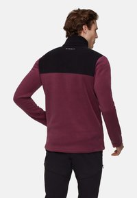 Bordowy polar z czarnym górnym panelem. Posiada wysoki kołnierz i ściągacze na mankietach. Logo tagu na tylnej części kołnierza. Gładka tekstura.