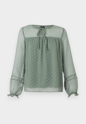 Sheer green blouse with polka dot pattern, round neckline, tie detail at front, and elasticized cuffs featuring decorative accents.