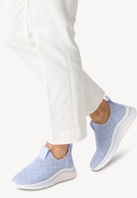 Ljusblå mesh-sneakers med en texturerad yta och vita gummisulor. Har en dragremsan och en sömlös design. Bärs med vita byxor.