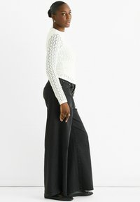 White knitted sweater with long sleeves and openwork design paired with high-waisted wide-leg black jeans and black flats.