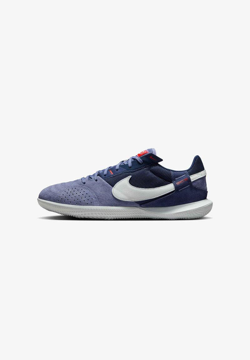 Ténis desportivos azul-marinho e azul-claro, feitos de camurça e malha, com um swoosh branco, solas texturizadas e detalhes em vermelho na língua.