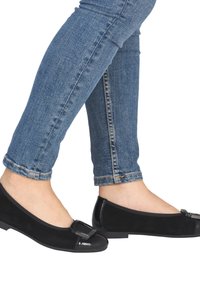 Ballerines noires en daim, dotées d'un bout en cuir verni brillant et d'une boucle décorative. Portées avec un jean bleu ajusté.