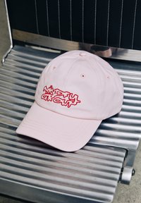 Casquette en coton rose avec visière incurvée, présentant un design de texte brodé rouge. Structure à six panneaux avec œillets de ventilation et sangle ajustable.