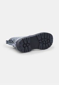 Bota de goma negra con una suela texturizada, que presenta un patrón de manchas blancas y grises. Incluye una tira para facilitar su uso.