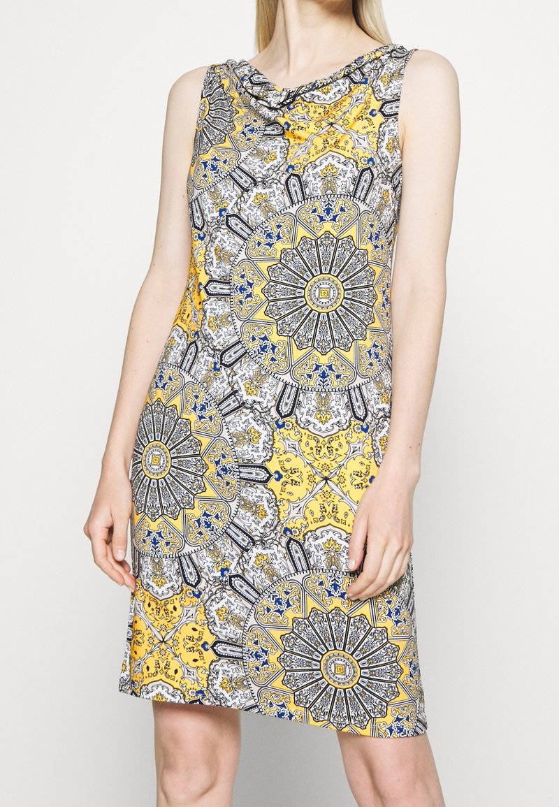 Robe sans manches avec un décolleté drapé, motif paisley complexe en jaune, noir et bleu, coupe à mi-genou et tissu léger.