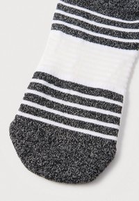Fekete-fehér csíkos zokni, texturált felső résszel, sima fehér középső szakaszával és egyszínű fekete alsó résszel. Puha szövetanyag.