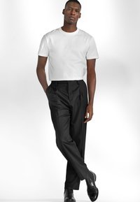 Vit bomullströja med korta ärmar, kombinerad med högmidjade svarta byxor och svarta läderskor, allt mot en ljus bakgrund.