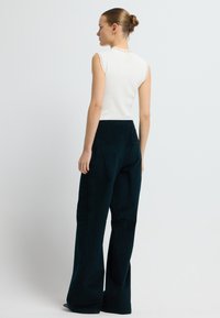 Bílý žebrovaný top bez rukávů s rýhovanými detaily na ramínkách, spárovaný s tmavě tyrkysovými širokými kalhotami z měkké, texturované tkaniny.