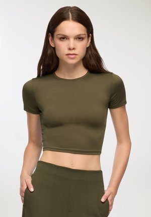 T-shirt cropped verde oliva con maniche corte, realizzata in tessuto morbido. Presenta un collo rotondo e un design aderente. Abbinato a pantaloni coordinati.