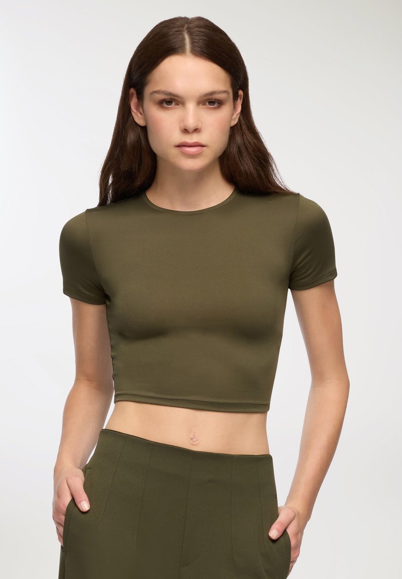 Oliwkowa krótka koszulka z krótkim rękawem, wykonana z gładkiego materiału. Posiada okrągły dekolt i dopasowany krój. W komplecie ze spodniami w tym samym kolorze.