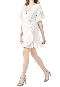 Vestido blanco de encaje con mangas rizadas, un lazo en la cintura y un dobladillo acampanado. Combinado con sandalias de tacón alto color nude con tiras.