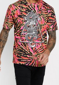 Tričko s krátkým rukávem v batikovaném vzoru růžové, černé a oranžové barvy, se středovým grafickým prvkem draka uvnitř trojúhelníku.
