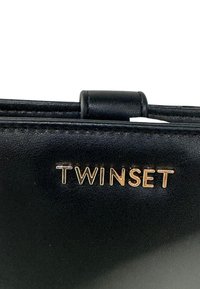 Primo piano di un oggetto in pelle nera con lettere in metallo dorato che compongono la scritta "TWINSET" su una superficie liscia.