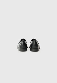 Chaussures en cuir noir avec une texture lisse, dotées d'un bout arrondi et d'un petit talon. Le design comprend des détails de couture discrets le long de l'arrière.
