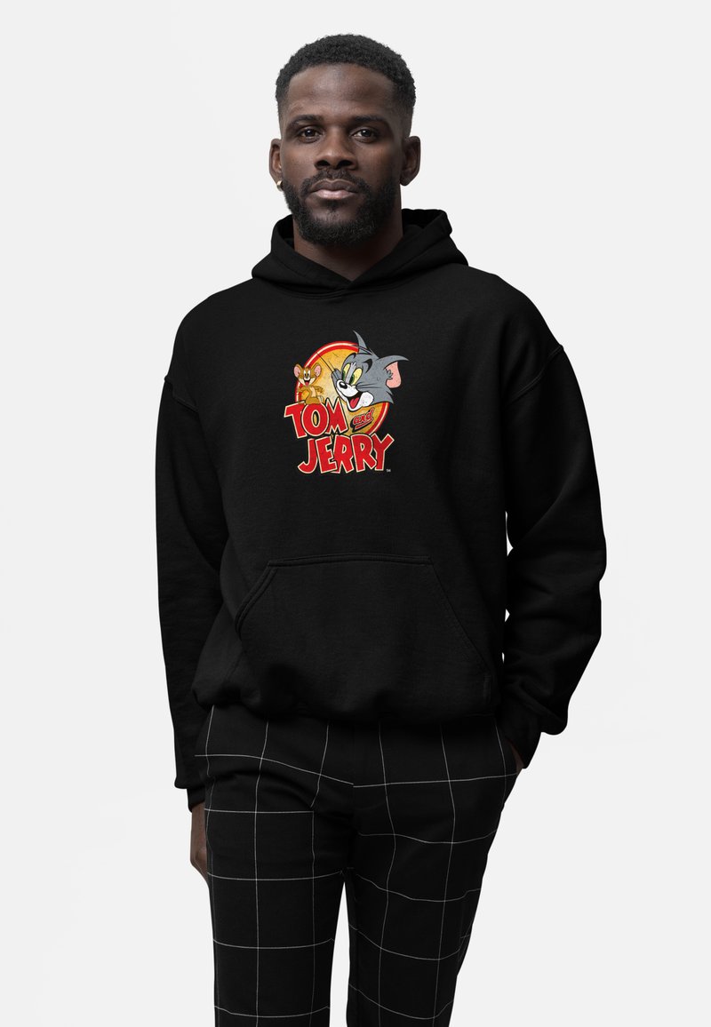 Czarna bluza z kapturem z kolorową grafiką przedstawiającą postacie Toma i Jerry'ego. Materiał wydaje się być miękki, a na przodzie znajduje się kieszeń.