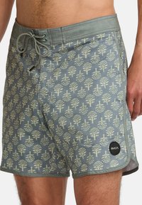 Shorts de baño para hombre en una tela azul-gris decorada con un patrón de árboles color crema. Cuentan con una cinturilla elástica con cordón y un bolsillo lateral.