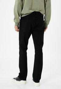 Jeans negros de corte recto, con bolsillos traseros y una textura suave. Combinados con un sudadera verde clara y zapatillas negras.