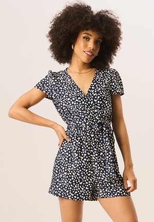 Navy romper with white heart-like spots, short sleeves, v-neckline, and a tied waist. Soft fabric with a smooth texture.