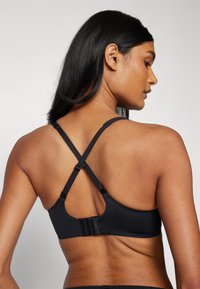 Black sports bra with a smooth texture, featuring crisscross straps and a hook-and-eye closure. Simple design with no patterns.