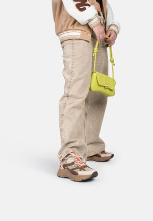 Beige collegejack, vervaagde beige jeans en multikleurige sneakers. Kleine felgroene handtas met een geknoopte band. Casual outfitdetails.