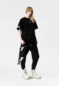 Camiseta negra de gran tamaño con un bolsillo frontal, combinada con pantalones jogger negros que tienen detalles gráficos en blanco, y botas de combate blancas y robustas.