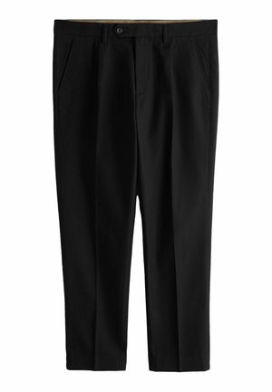 Bărbat purtând pantaloni negri plisati și o cămașă albă cu mâneci lungi și nasturi, cu mâna stângă sprijinită lângă pantaloni.