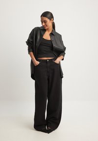 Svart läderoversized skjorta, svart linne och vida jeans. Spetsiga svarta skor med rosett detaljer. Enkel, monotonk design.