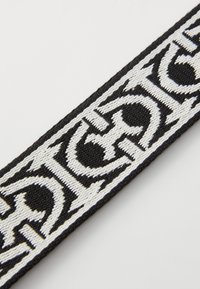 Mustmustri nöör, millel on valget värvi broderitud tekst ja keerukad mustrid, esitleb tekstureeritud pinda ja julgeid kujunduselemente.