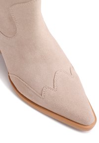 Μπεζ σουέντ μπότα με μυτερή μύτη και διακοσμητικό ράψιμο κατά μήκος της μπροστινής άκρης και του πλαϊνού πάνελ, ορατή λεία ταμπά σόλα.