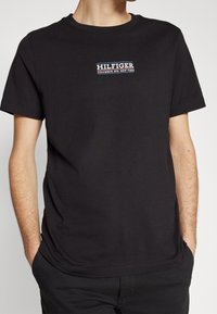 Černé bavlněné tričko s krátkým rukávem, zdobené vyšitým logem v červené, bílé a modré barvě s textem "HILFIGER COLUMBUS AVE. NEW YORK".