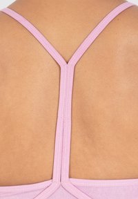 Vaaleanpunainen rintaliivi, jossa kapeat hihnat muodostavat V-muotoisen selkäosan. Sujuva pinta, joka sopii vaalealle ihonvärille. Yksinkertainen, toiminnallinen muotoilu.