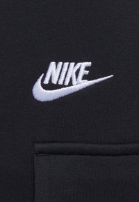 Černá tkanina s hladkou texturou, která obsahuje výrazné bílé vyšívané logo Nike a malý detail kapsy.