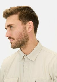 Hellbeige Hemd mit Kragen, Knopfverschluss und zwei Brusttaschen, das eine glatte Textur und ein minimalistisches Design aufweist.
