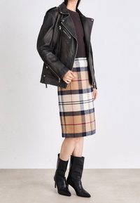 Veste de motard en cuir noir, haut ajusté marron, jupe crayon en plaid beige avec des accents bleu marine et rouge, bottes noires à talons hauts jusqu'aux genoux.