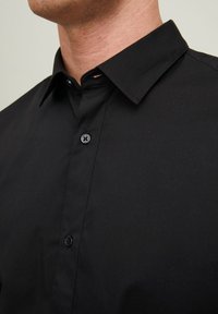 Camicia in cotone nera con colletto classico, caratterizzata da una superficie liscia, un leggero lucido e una chiusura con un singolo bottone.