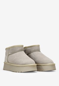 Stivali ankle in suede beige con punta arrotondata, suola in gomma piatta e dettagli cuciti lungo la cucitura e il colletto.