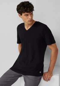 Czarny krótki rękaw T-shirt z dekoltem w serek, wykonany z lekkiego materiału. Posiada prosty krój dolnej krawędzi oraz niewielką metkę z logo w lewym dolnym rogu.